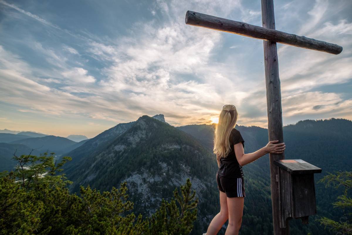 Eine Frau steht neben dem Gipfelkreuz und blickt auf die Berge nahe des Wanderhotels in Bayern Gut Steinbach