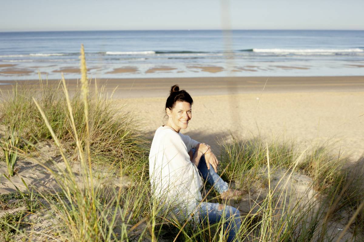 Yogalehrerin Andrea Schwarz sitzt an der Seeküste und lächelt in die Kamera