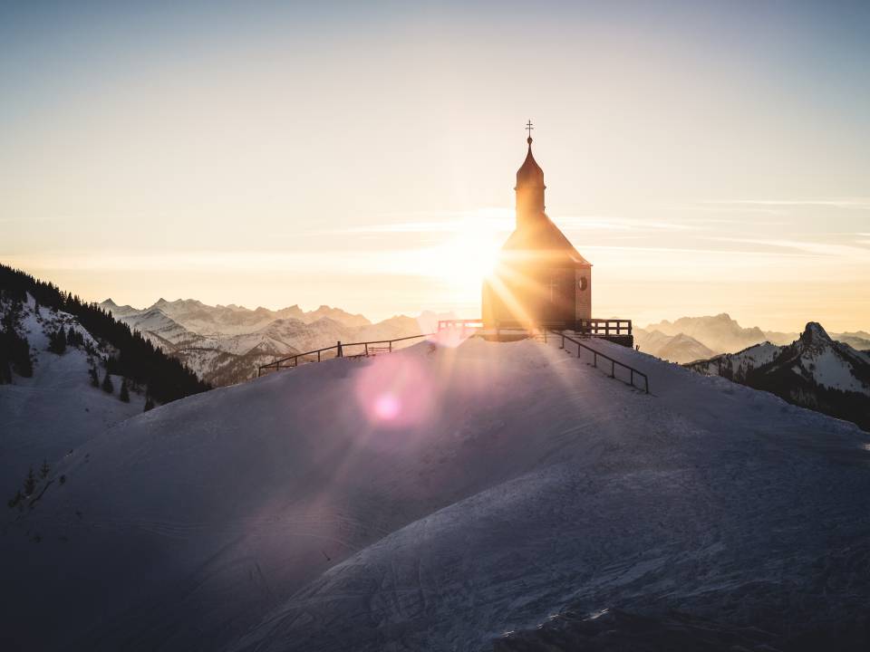 Sonne blitzt an einer kleinen Kirche vorbei, die auf einem verschneiten Berg steht