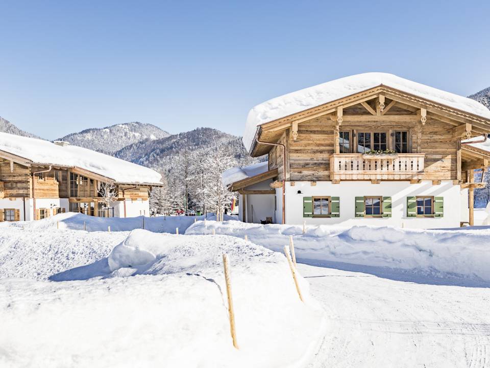 Mehrere verschneite Chalet-Häuser stehen neben einem gepflügten Weg