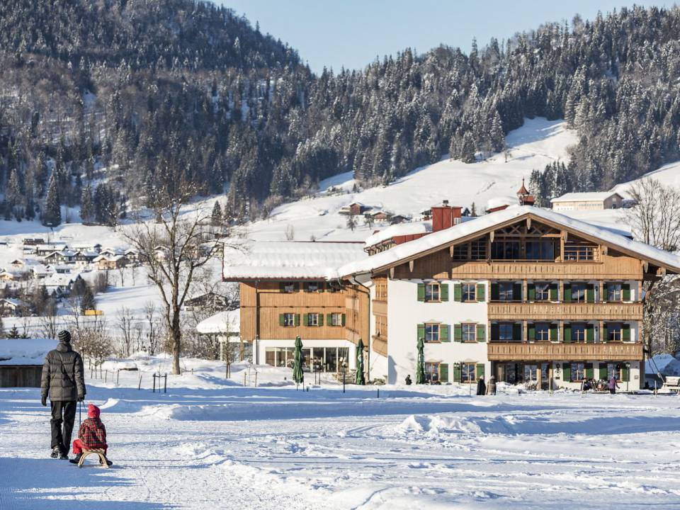 Kind rodelt in Reit im Winkl neben ihrem Vater den Berg runter