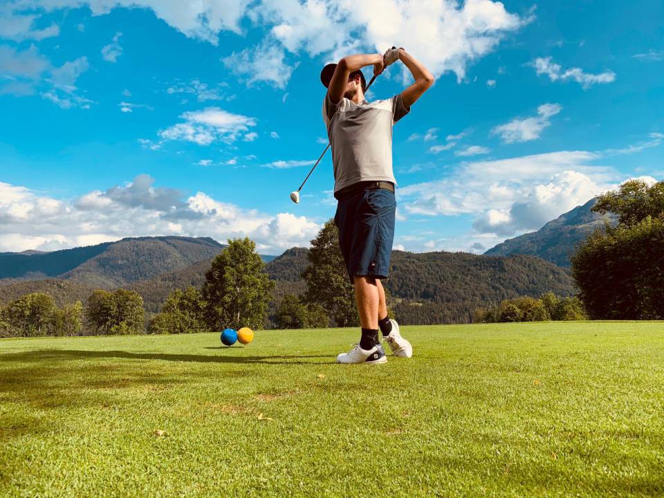 Ein Mann, der seinen Golfschläger schwingt, um einen gelben und einen blauen Ball auf dem Golfplatz nahe des Golfhotels in der Region Chiemsee zu schlagen
