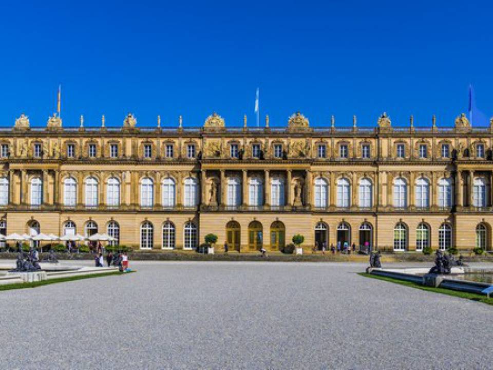 Frontaler Blick auf das Schloss Herrenchiemsee und den Vorplatz bei blauem Himmel