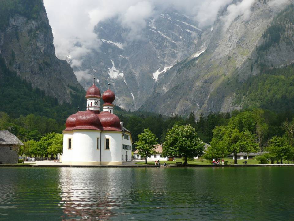 Die Wallfahrtskirche St. Bartholomä mit rotem Dach befindet sich direkt am Königssee, im Hintergrund sieht man Berge