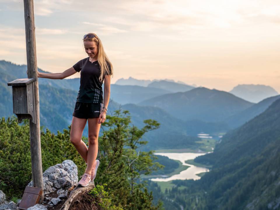 Eine Frau am Berggipfel mit Ausblick über das Tal nahe des Wanderhotels in Bayern