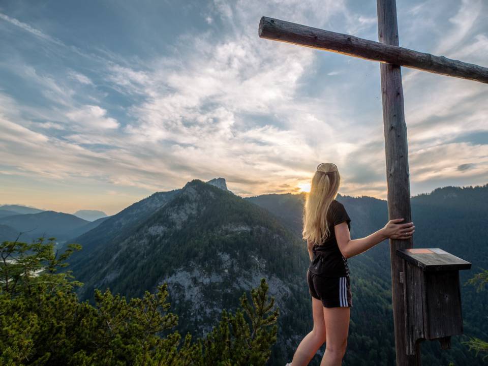 Eine Frau steht neben dem Gipfelkreuz und blickt auf die Berge nahe des Wanderhotels in Bayern Gut Steinbach