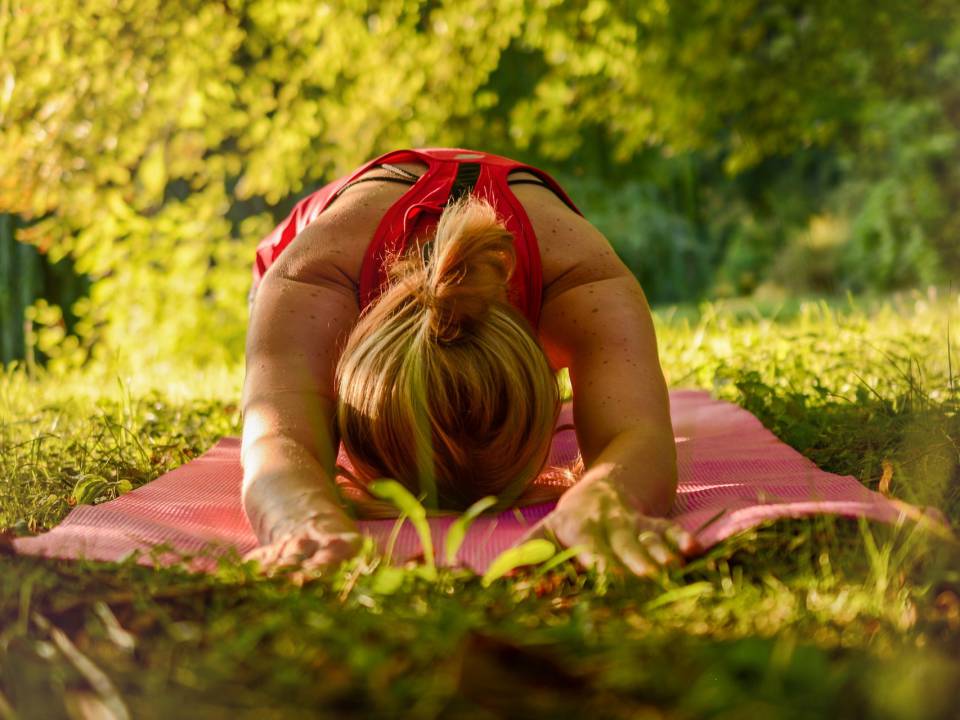 Dame macht ein Yoga Retreat auf einer Wiese am Chiemsee und streckt sich auf einer roten Matte