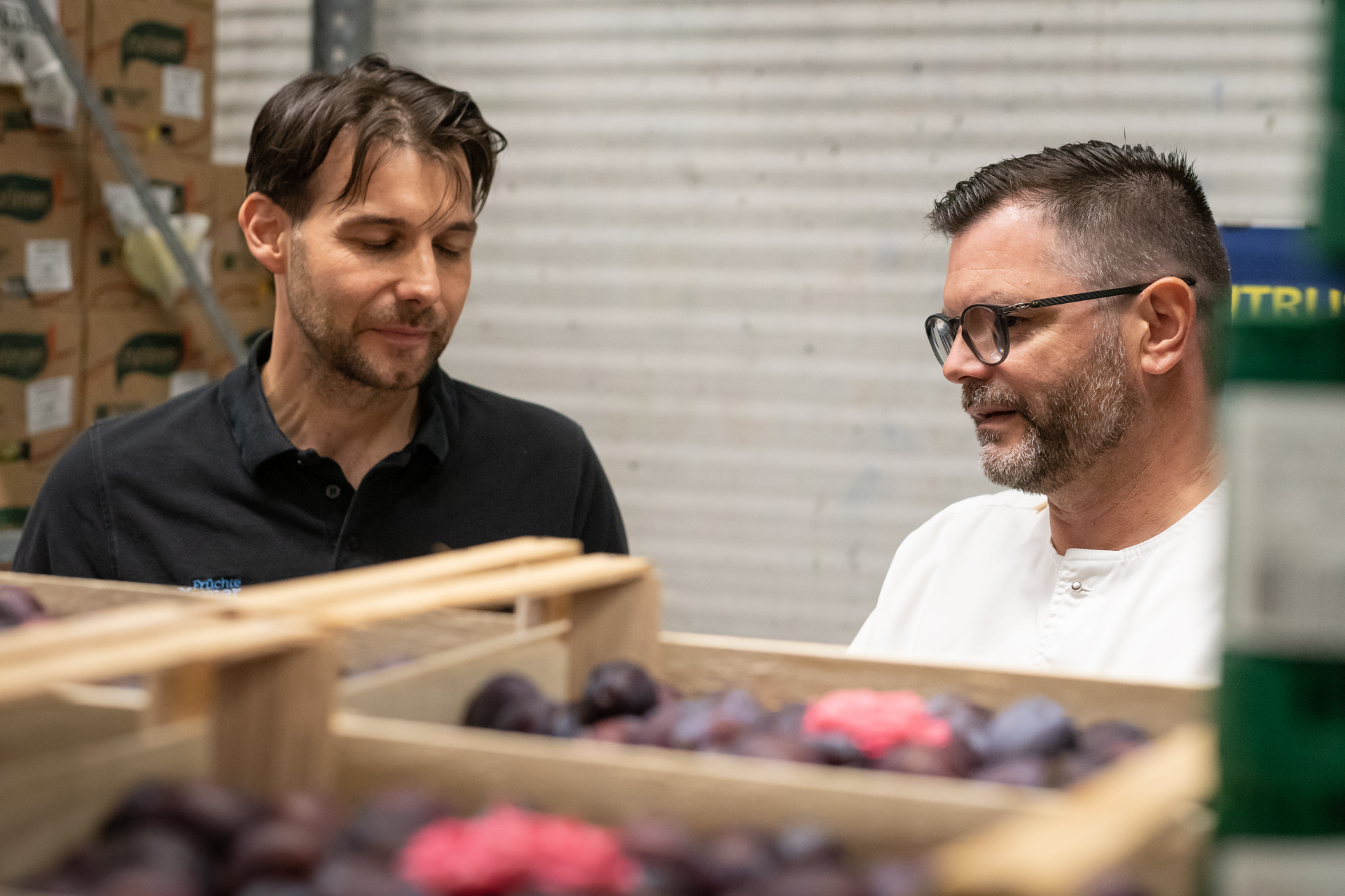 Herr in weißer Kochjacke nimmt seinem Lieferanten die Obstware ab