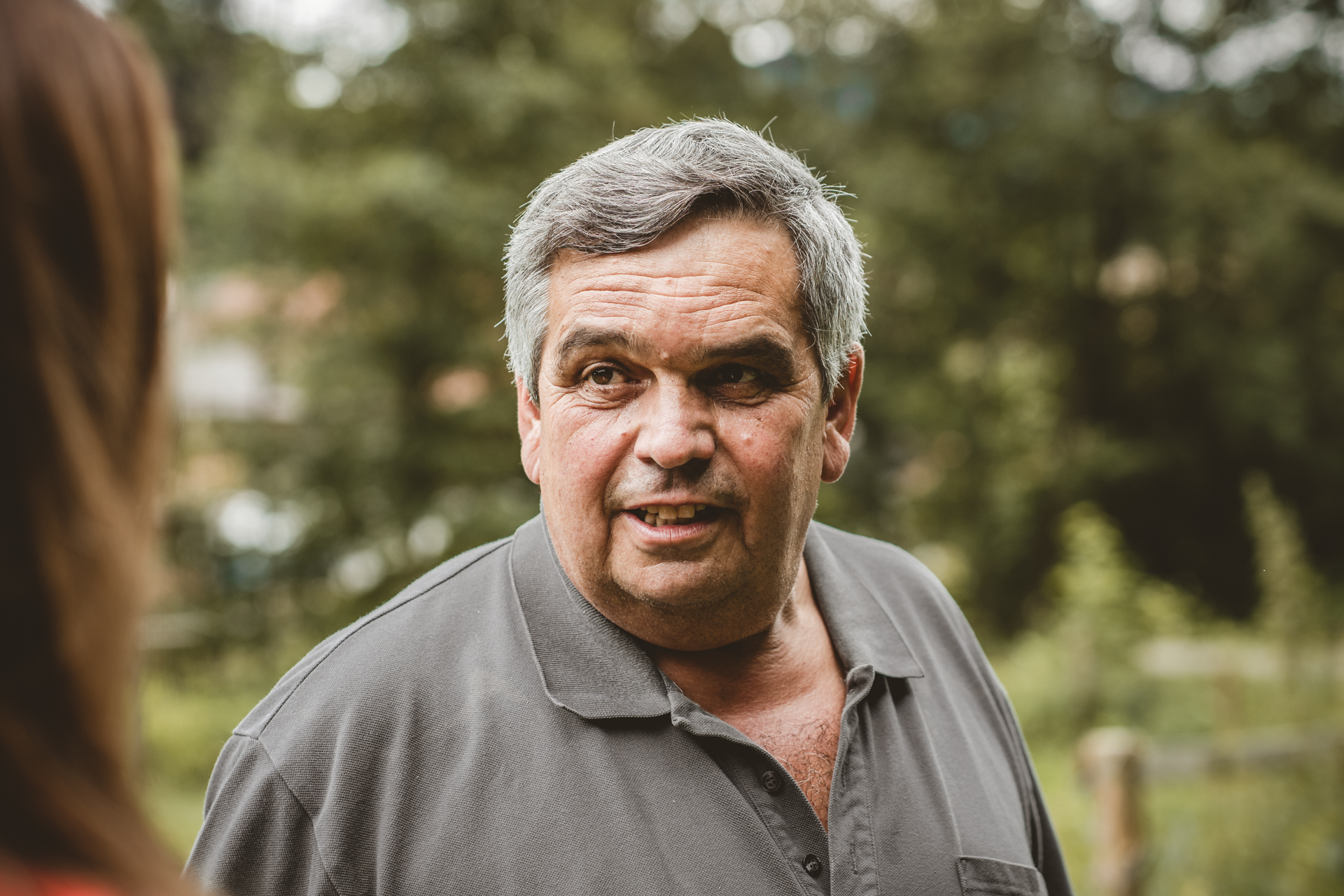 Ein Herr in grauem Polo-Shirt unterhält sich mit einer Frau, die mit dem Rücken zur Kamera steht